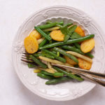 Overhead view of Green Beans with Crispy Potatoes on a decorative white plate on a white table