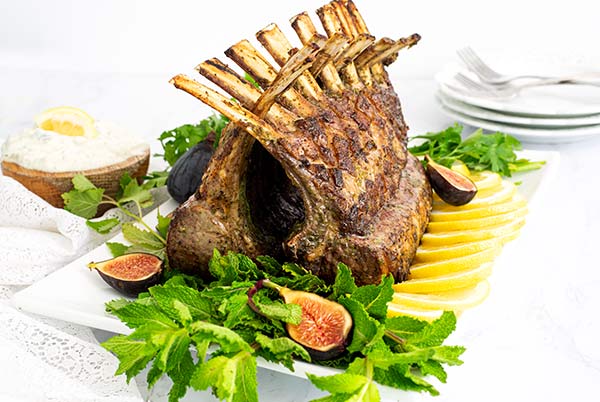 Mint and Herb Rack of Lamb on a white rectangular platter garnished with lemon slices and mint and figs