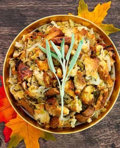 Overhead view of Mom's Stuffing in a gold bowl on a dark wood table with orange maple leaves under the bowl and sage garnish