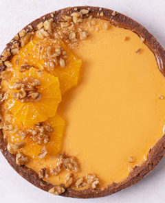 Overhead view of No-Bake Pumpkin Orange Pie with walnuts and oranges on top on a white table