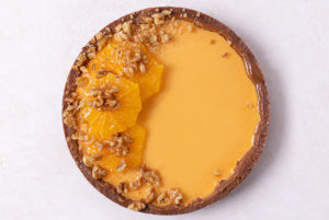 Overhead view of No-Bake Pumpkin Orange Pie with walnuts and oranges on top on a white table