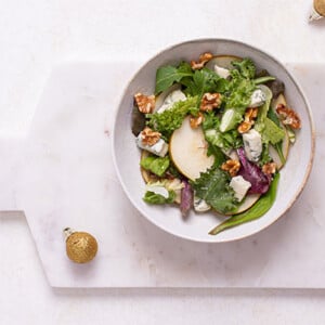 Overhead view of Pear Salad with Blue Cheese Honey Vinaigrette in a white bowl on a white marble cutting board
