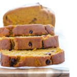 Close-up of Pumpkin Cranberry Bread sliced on a wooden cutting board against a white background