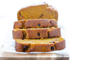 Close-up of Pumpkin Cranberry Bread sliced on a wooden cutting board against a white background