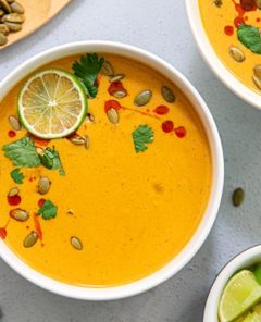 Overhead view of Thai Pumpkin Soup in white bowls garnished with lime slices and pumpkin seeds on a gray background