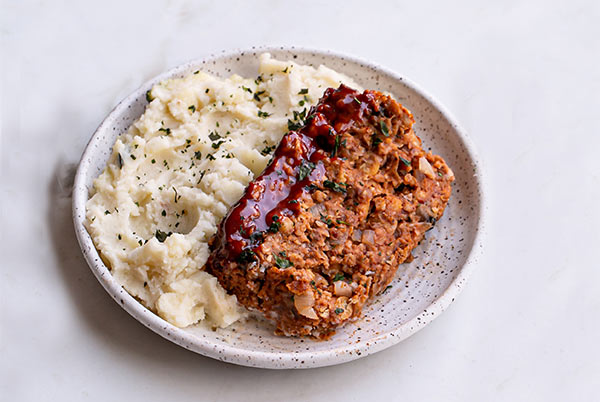 Vegan Meatloaf with mashed potatoes on a white speckled plate on a white background