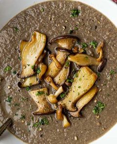 Overhead view of Wild Mushroom Bisque in a white bowl with sauteed trumpet mushrooms on top as garnish