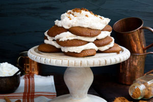 Ginger Snap Icebox Cake on a white cake stand against a dark gray background with copper cups in the background