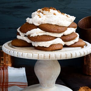 Ginger Snap Icebox Cake on a white cake stand against a dark gray background with copper cups in the background