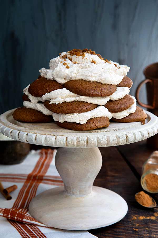 Closeup of Ginger Snap Icebox Cake on a white cake pedestal on a dark wood table with dark gray background and white and copper colored cloth napkin