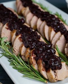 Pork Tenderloin with Cranberry Rosemary Sauce arranged on a white rectangular platter with rosemary garnish