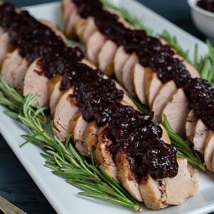 Pork Tenderloin with Cranberry Rosemary Sauce arranged on a white rectangular platter with rosemary garnish