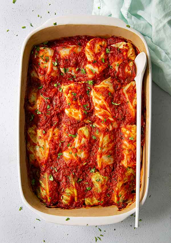 Overhead view of Stuffed Cabbage Rolls in a rectangular casserole dish with a pale teal cloth napkin on the side