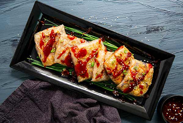 Overhead view of Turkey Rice Paper Dumplings with Cranberry Dipping Sauce on a black rectangular plate on a dark gray wood table