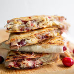 Turkey and Cranberry Quesadillas stacked on top of each other on a wooden cutting board with fresh cranberries on the sides