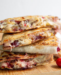 Turkey and Cranberry Quesadillas stacked on top of each other on a wooden cutting board with fresh cranberries on the sides