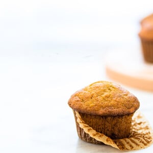 Front view of a Banana Muffin with two banana muffins out of focus to the right on a riser.