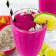 An overhead view of the dragon fruit smoothie with a black and white striped straw in it with a lime on the rim.