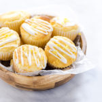 An overhead view of Lemon Ricotta Muffins in a wooden bowl with wax paper under the muffins