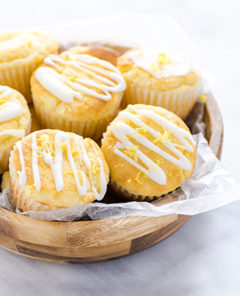 An overhead view of Lemon Ricotta Muffins in a wooden bowl with wax paper under the muffins