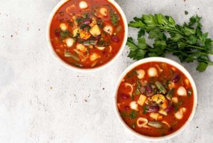 An overhead view of two bowls of Minestrone Soup with parsley on the right side of the bowls.