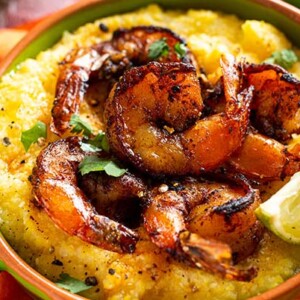 A up close overhead view of a Taco Shrimp and Polenta Bowl in a green bowl with an orange cloth napkin underneath the bowl.