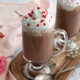 two Vanilla hot chocolates in glass with whipped cream and sprinkles on top on a wooden tray