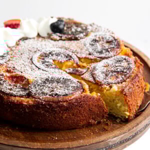 The blood orange olive oil cake on a wooden serving tray with a slice cut out of it.