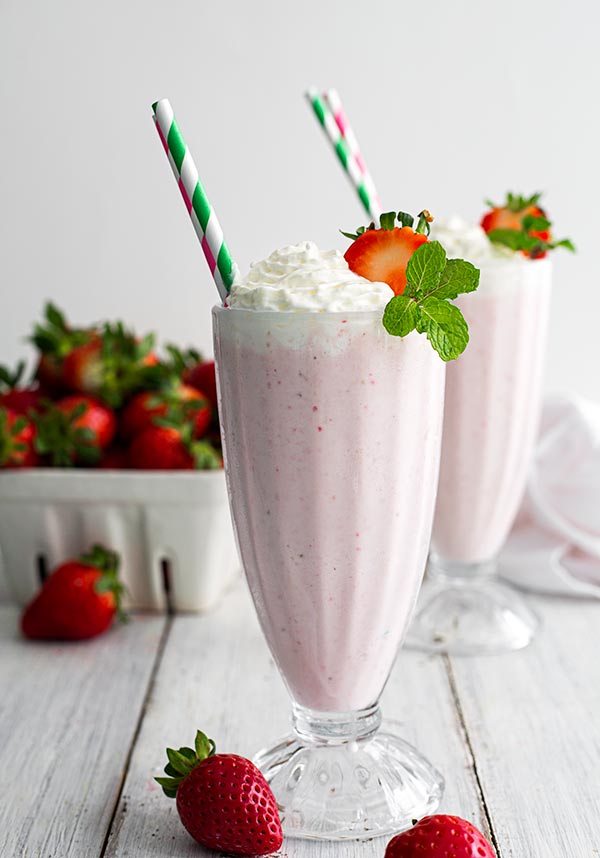 two boozy strawberry milkshakes with a straw in it. 