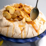 The Brown Sugar Pavlova on a blue serving tray with a spoon drizzling caramel sause on top of it.