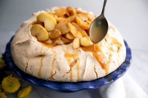 The Brown Sugar Pavlova on a blue serving tray with a spoon drizzling caramel sause on top of it.
