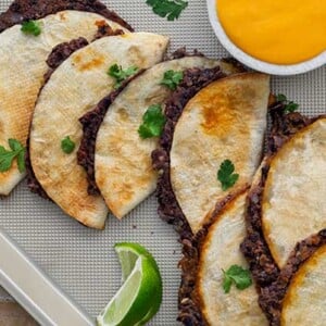 an over head view of the crispy plant based bean tacos on a tray next to cheese dip and a lime.
