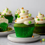 Green velvet cupcakes decorated with sprinkles on a white platter.