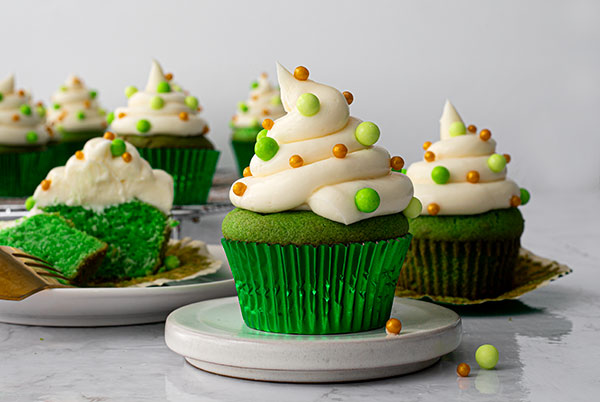 Green velvet cupcakes decorated with sprinkles on a white platter.