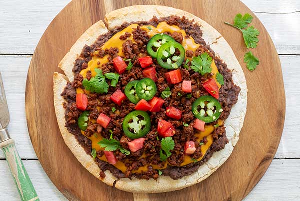 a whole plant-based nacho pizza on a wooden serving tray